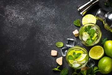 Obraz na płótnie Canvas Mojito cocktail with ingredients on black stone background. Summer drink mojito with lime, rum, mint and ice. Top view copy space.