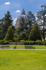 Obraz premium Inner courtyard of Vatican city museum with visitors and St. Peters church Dome visible in background. Beautiful popes garden, with green grass and trees Vatican, Rome, July 7, 2021