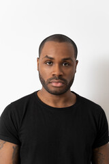 Fototapeta premium Portrait of an attractive African-American millennial man, a handsome young man in a black T-shirt, a serious boy looking into the camera, a student posing isolated in the studio.