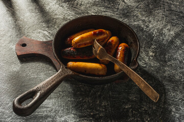Still life in a rustic style- fried sausages in a cast-iron pan on a dark background