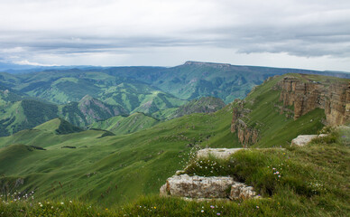 Fototapeta na wymiar Dramatic landscape - panoramic view of the hilly valley from the Bermamyt plateau in Karachay-Cherkessia in a misty haze and stone cliffs