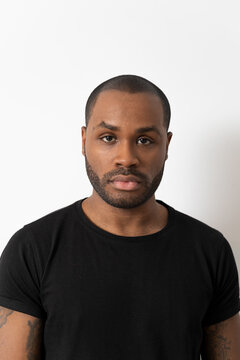 Portrait of an attractive African-American millennial man, a handsome young man in a black T-shirt, a serious boy looking into the camera, a student posing isolated in the studio.