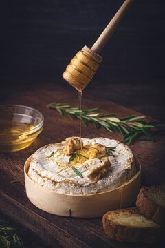 French cheese Camembert baked in a wooden box served with honey, aromatic herbs and nuts. Taste of France, rustic style. Pouring honey on cheese