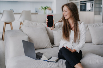 Laughing blond Italian girl in suit works at home using laptop shows switched off phone realised that was talking with no-one. Funny situation. Remote working Italian businesswoman. Business people.