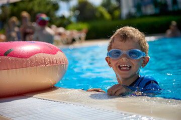 Cheerful boy in swimming glasses swims in a summer pool with an inflatable circle. Funny kid having...