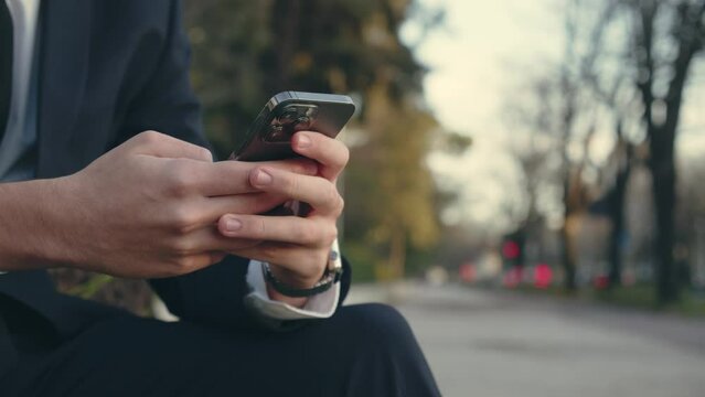 Close up Male hands with smartphone, outdoors. Human holds cell phone close up,  slow motion footage. Businessman is typing text messages on mobile phone sitting in the park