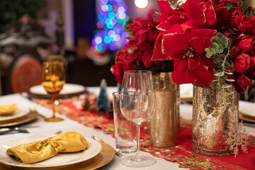 Table de fête avec couverts et verres de luxe, serviettes, assiettes et vases dorés, nappe...