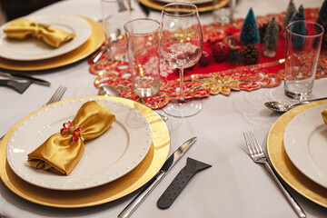 Table de fête avec couverts et verres de luxe, serviettes et assiettes dorées. Décoration de Noël et napperon brodé rouge. 