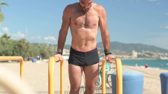 Front view of brunette man practicing calisthenics on parallel bars. Sports concept.