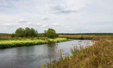 A beautiful pastoral landscape - the bend of the Klyazma River among the picturesque banks in the Moscow region with green grass and trees and a cloudy sky and a space to copy