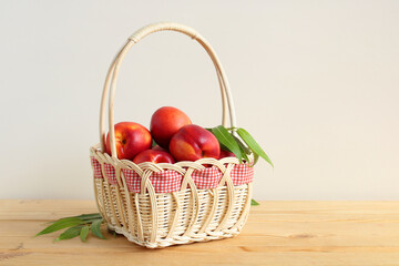 basket of nectarines with leaves on the table on a light background in the room.