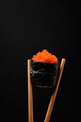 Gunkan Maki Sushi with red flying fish roe and chopsticks on black background