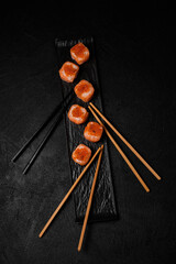 salmon sushi roll with red caviar and chopsticks for three person on top on black concrete