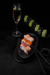 Different kind of sushi roll; chopsticks and glass of shampagne on black background