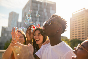 Group of multiracial happy friends having fun with soap bubbles in the city - Cheerful young...