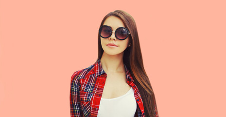 Portrait of beautiful young brunette woman wearing sunglasses on pink background