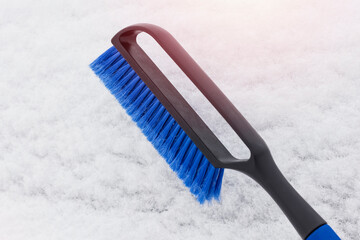 Blue brush for cleaning the car from snow. Detail of a cleaning tool on a background of white snow. Close-up