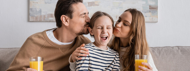 parents holding glasses of orange juice and kissing head of daughter at home, banner.