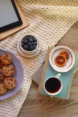 Plate of cookies, cup of tea, fresh blueberries, dry oranges, stack of books, reading glasses and tablet on the table. Hygge at home. Flat lay.