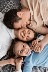 top view of joyful parents and happy kid lying on bed at home.