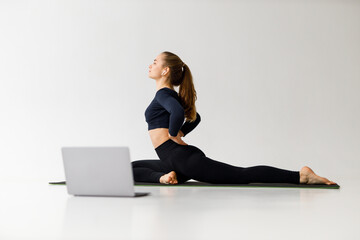Personal trainer conducts online yoga class, young woman practices stretching training session.