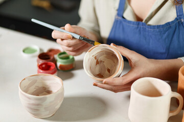 Woman hands, pottery studio and painting cup in workshop for sculpture, creative manufacturing or design. Painter, ceramics product and brush process, artistic pattern or production in small business