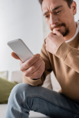 low angle view of man in beige jumper messaging on smartphone at home.