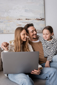 happy parents holding hands near daughter looking at laptop in living room.