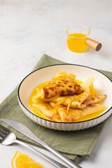 Dessert, thin pancakes with orange caramel and zest or crepe suzette on a white plate on a light concrete background. French cuisine. International pancake day.