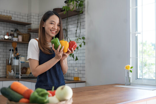 Portrait of young happy woman wearing appron standing in the kitchen room, prepares cooking healthy food from fresh vegetables and fruits.