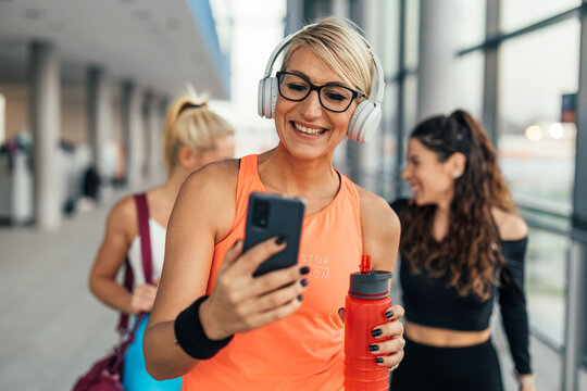 Front view of a blonde middle-aged woman having a video call in the gym