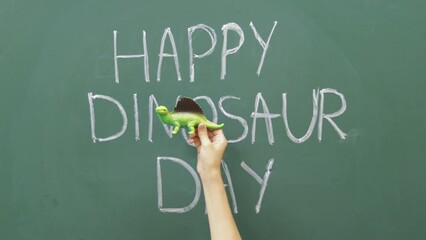 happy dinosaur day words written on blackboard with white chalk and woman girl hands playing with 2 two dinosaurs walking in front of each other having fun crazy celebration may 15th june 1st