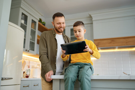 Father with son using digital tablet together at home kitchen