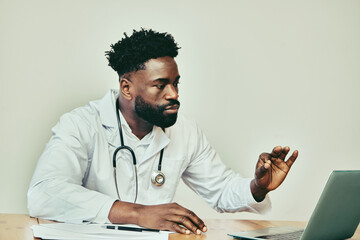 African American doctor on video call consultation, seated at desk with laptop