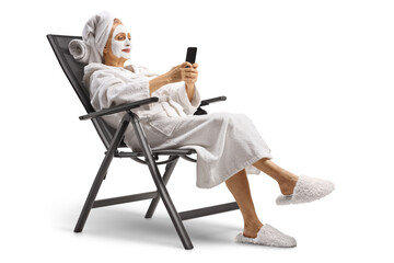 Woman with a cosmetic face mask sitting and using a smartphone