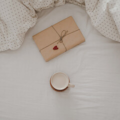 Cup of coffee with milk and gift box in bed with plaid, copy space. Flat lay, top view. morning in bed concept composition