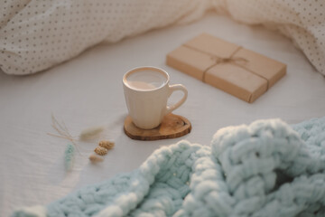 Cup of coffee with milk and gift box in bed with plaid, copy space. Flat lay, top view. morning in bed concept composition