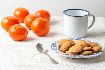 Top view of cookies, cup of coffee, spoon and tangerines on white tablecloth, horizontal with copy...