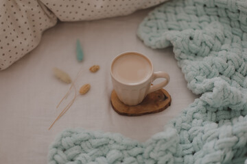 Cup of coffee with milk on the bed with white linens and blanket. Morning coffee in bed concept.