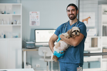 Happy young male veterinarian in blue uniform holding yorkshire terrier
