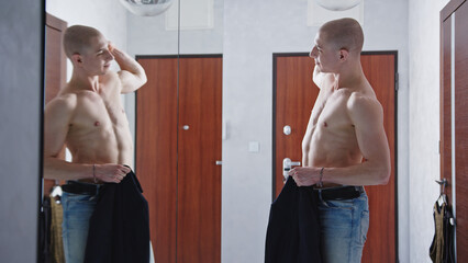 Muscular bald man with shirtless torso flexing biceps in front of a mirror. High quality photo