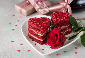 Cakes Red velvet in the shape of hearts on white plate, rose and bottle champagne for Valentines Day on gray background