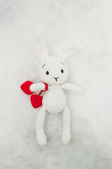 A white knitted bunny holds red hearts on a gray background.