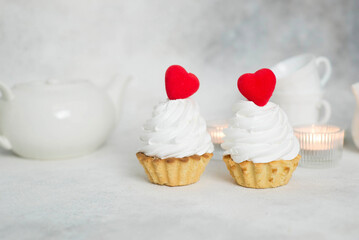 two cakes with red hearts and teapot, cups, candles on a gray background.