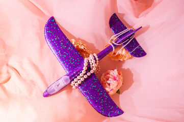 Purple children's plane lies among the flowers surrounded by beads and dramatic shadows.