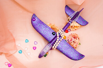 Purple children's plane lies among the flowers surrounded by beads and transparent colored hearts