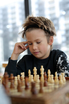 a boy of eight years, Caucasian appearance, sits in a bright room, plays chess with a friend. The boy is focused, thinks through the moves