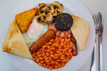 White board with full English breakfast with bacon, fried egg, beans, tomato, roasted sausage,...