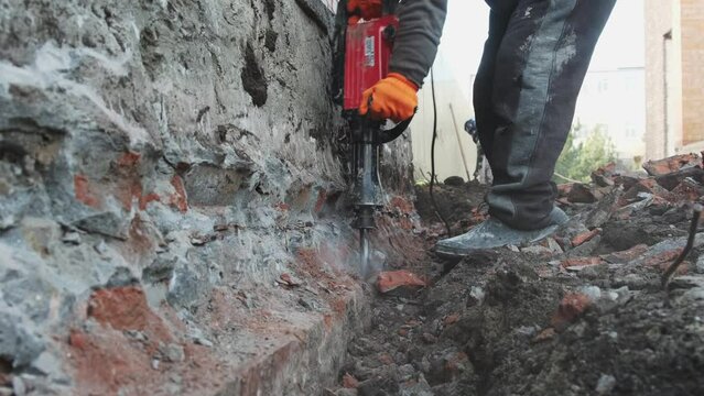 Workers use an electric jackhammer to break off an old foundation. Construction of a new residential building.