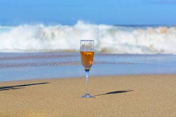 One glass of rose champagne or cava sparkling wine served on white sandy beach and blue ocean water, romantic vacation, winter sun on Fuerteventura, Canary, Spain